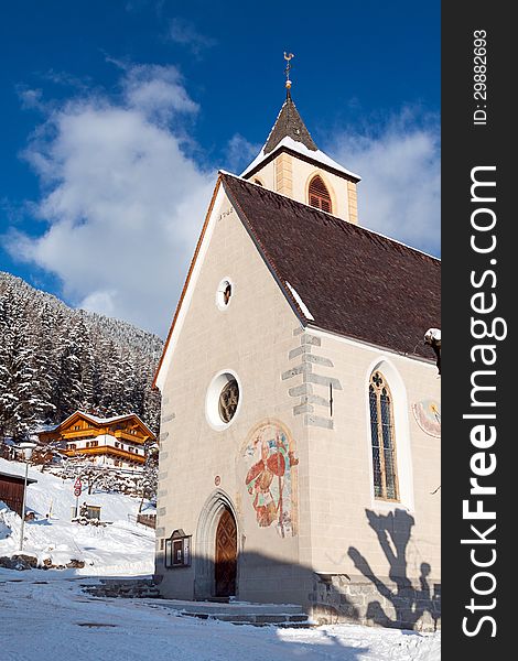 A wintertime view of a small church with a tall steeple in Vila di Sopra, Sud Tyrol