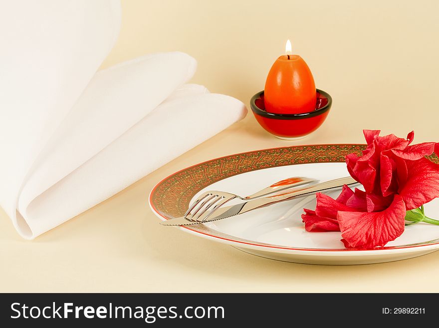 Table setting by Easter - a dish with knife and fork decorated with red flower, Easter candle and napkin