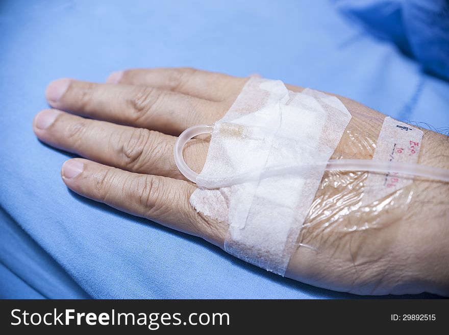 Old man hand with IV in hospital's bed