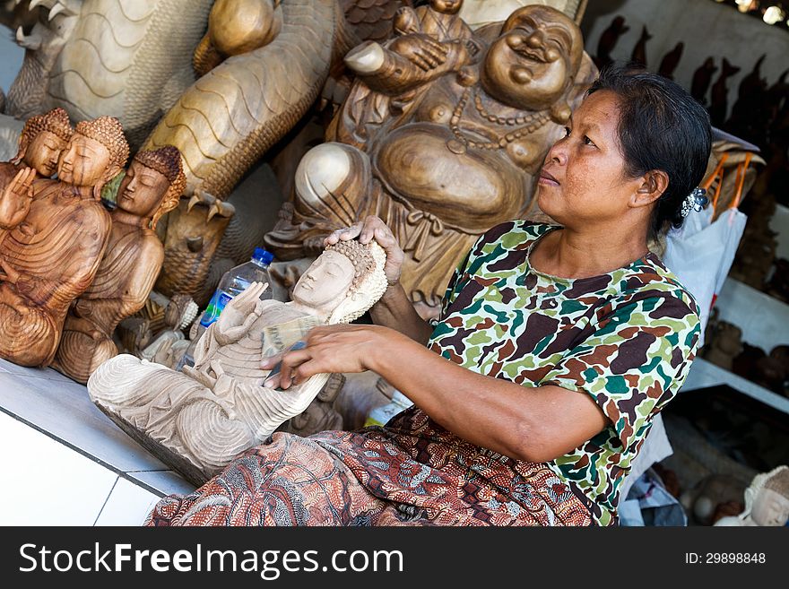 A woman is polishing wooden Buddha in Indonesia