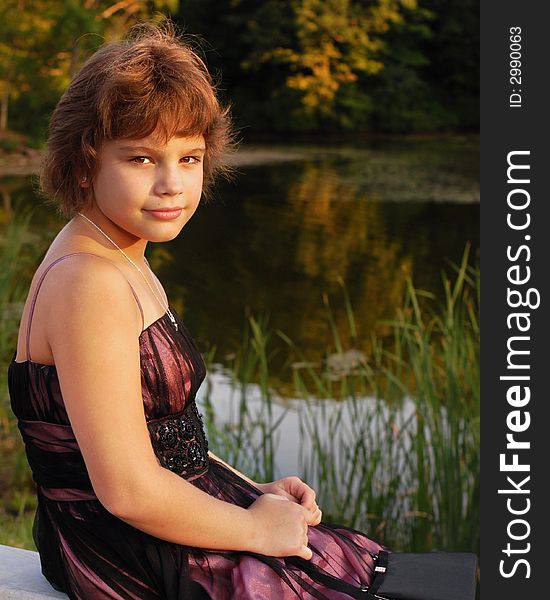 Elementary girl in formalwear looking at the viewer from a pond in late afternoon. Elementary girl in formalwear looking at the viewer from a pond in late afternoon.