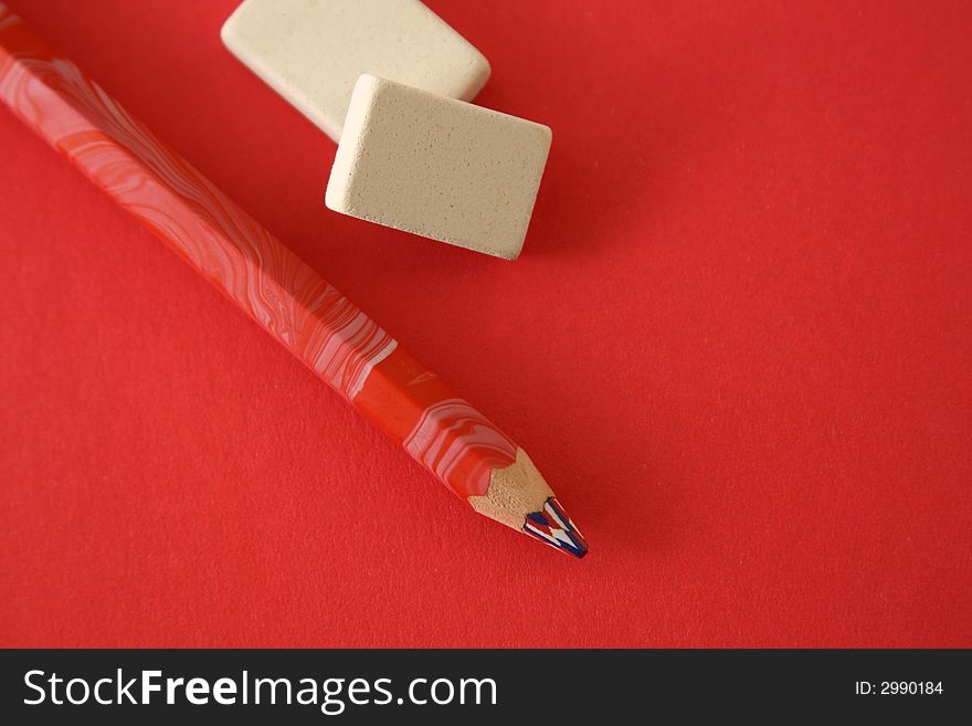 Pencil and two erasers on a red background