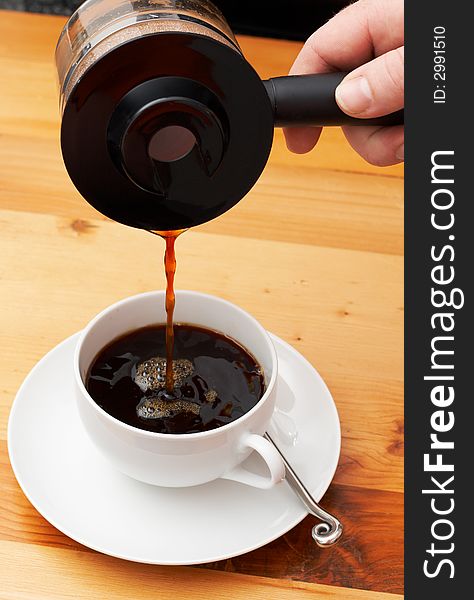 Closeup of coffee being poured from the pot into the cup. Shot on light wood background