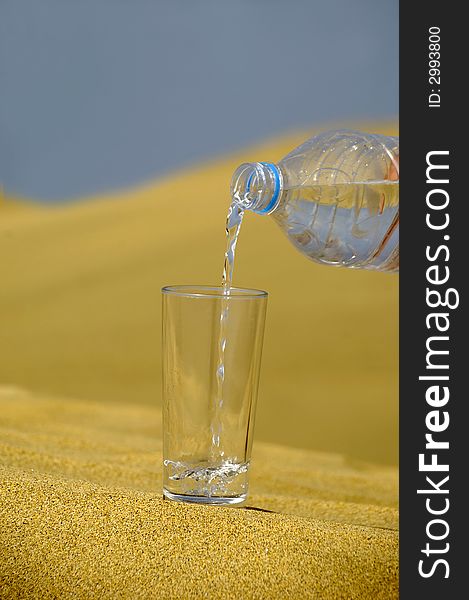 A glass of fresh water and bottle in a desert. A glass of fresh water and bottle in a desert