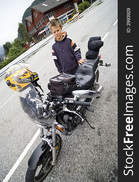 A boy standing next to a motorbike, looking at it with admiration. Wide angle view. A boy standing next to a motorbike, looking at it with admiration. Wide angle view.
