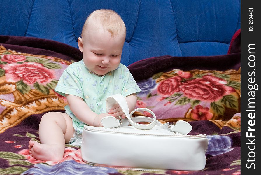 Child sitting on a bed plays with a white female bag. Child sitting on a bed plays with a white female bag