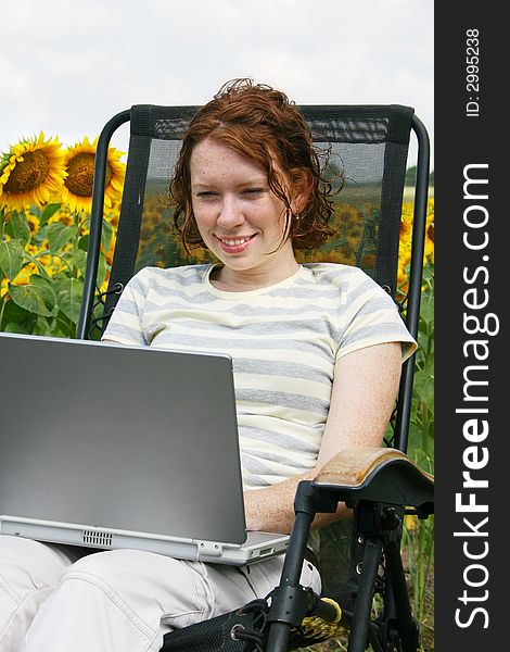 A young lady working on her laptop by a field of sunflowers. A young lady working on her laptop by a field of sunflowers