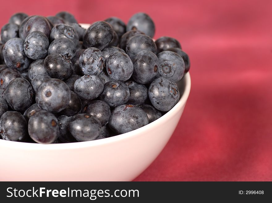 Blueberries in a white bowl with a wine colored background. Blueberries in a white bowl with a wine colored background