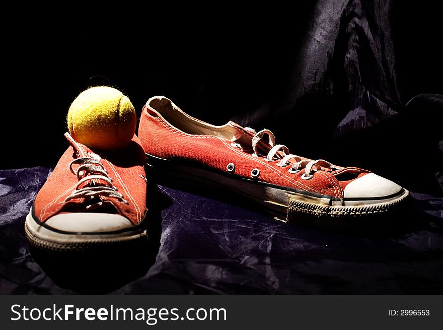 Red old sneakers and tennis ball on the dark blue background