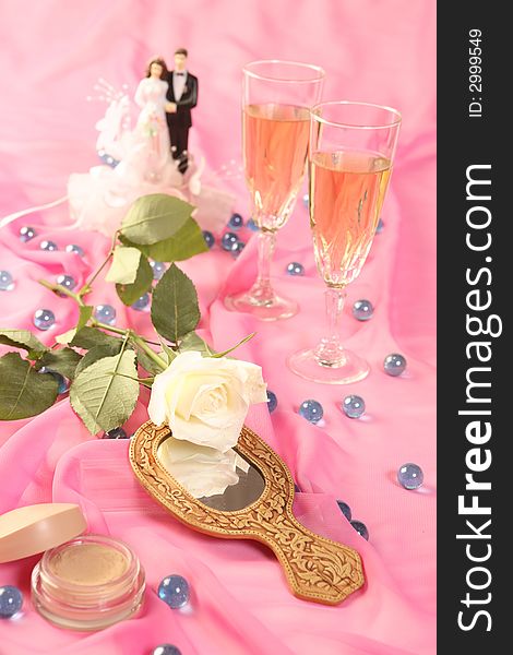 A photo of wedding cake dolls, rose and glasses over pink