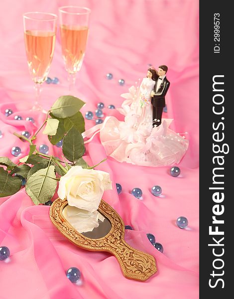 A photo of wedding cake dolls, rose and glasses over pink