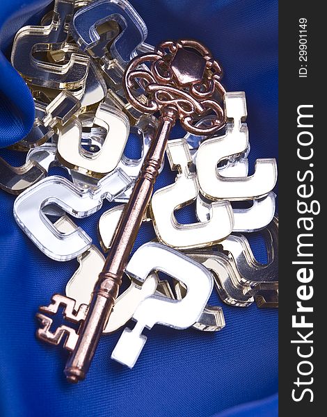 Key to all questions concept shot with gold and silver question marks, vintage skeleton key on a blue silk background.