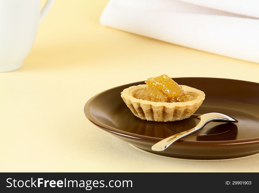 Tartlet with peach jam on brown saucer, on a light background