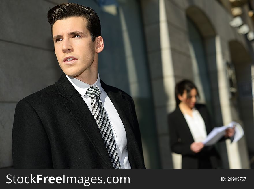 Portrait of attractive young businessman in the city with beautiful businesswoman in the background. Portrait of attractive young businessman in the city with beautiful businesswoman in the background