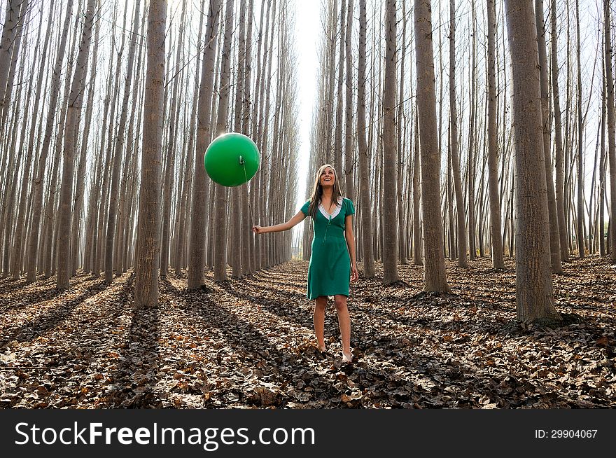 Portrait of beautiful blonde girl, dressed in green, walking into the forest