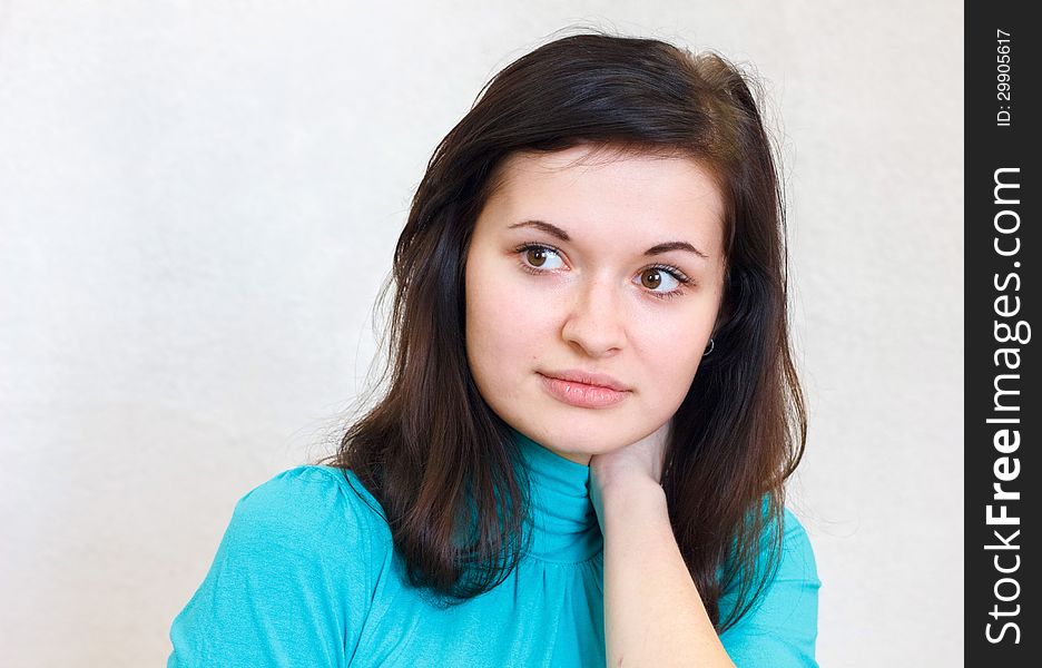 Close-up portrait of a young beautiful brunette girl thoughtfully looks aside in the blue sweater