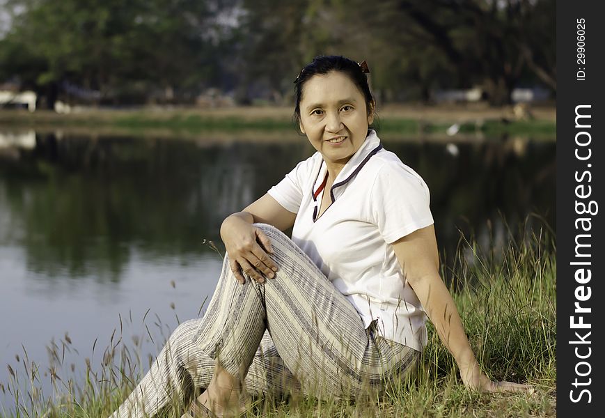 Woman sitting on green field by lake