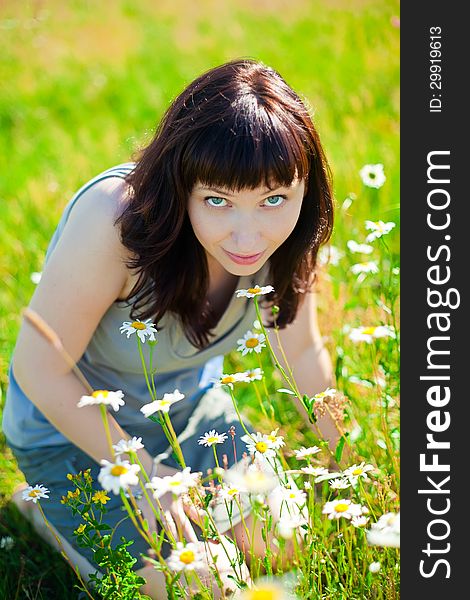 Beautiful dark-haired smiling woman sitting on a grass, smelling camomiles. Beautiful dark-haired smiling woman sitting on a grass, smelling camomiles