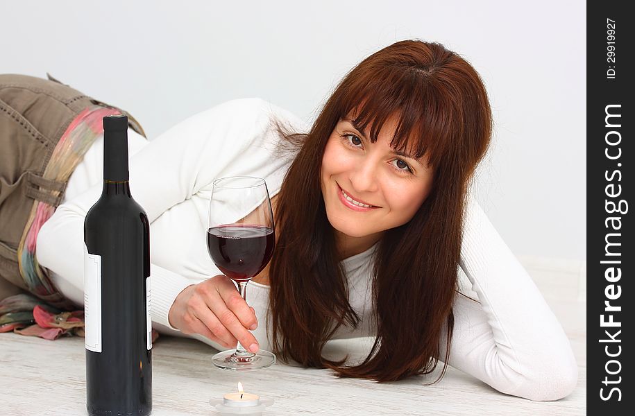 Beautiful, smiling woman relaxing with glass of red wine on the floor
