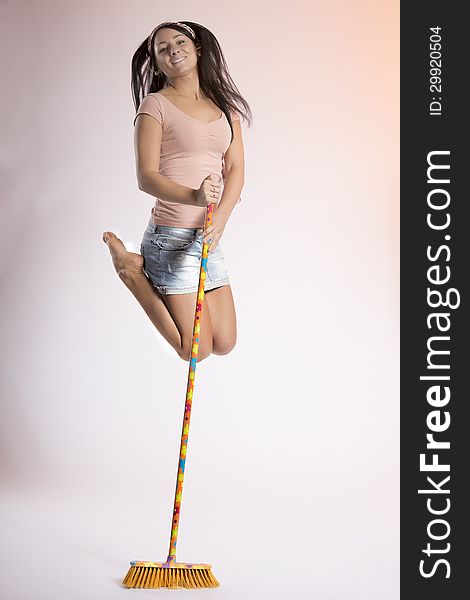 Cute brunette girl in mini jeans skirt jumps high holding to a broom. Cute brunette girl in mini jeans skirt jumps high holding to a broom