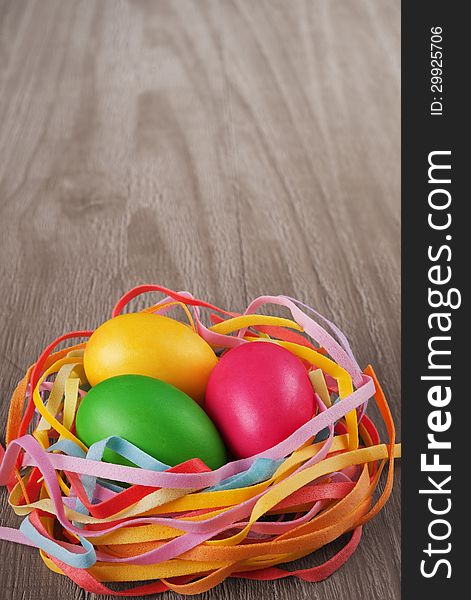 Multicolored easter eggs in the nest on old wooden table