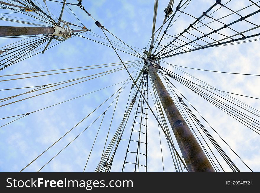 Two wooden ship masts with ropes over blue cloudy sky