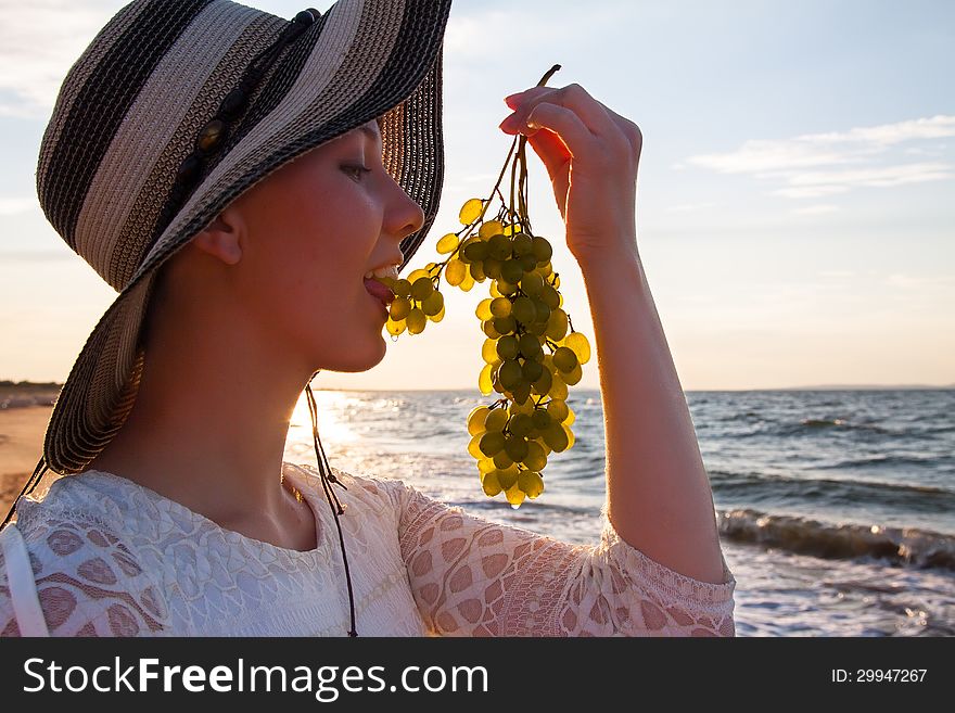 Beautiful young woman in hat at sea shore holding grapes. Beautiful young woman in hat at sea shore holding grapes