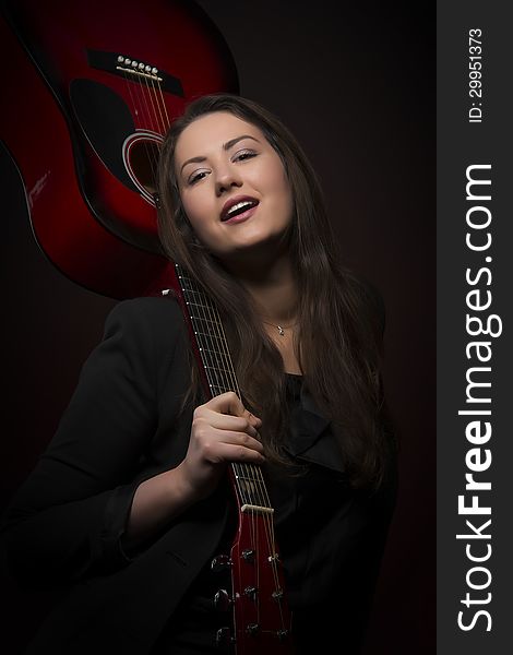 Portrait of young self-confident expressive woman holding red color guitar upside down, isolated on dark background. Portrait of young self-confident expressive woman holding red color guitar upside down, isolated on dark background