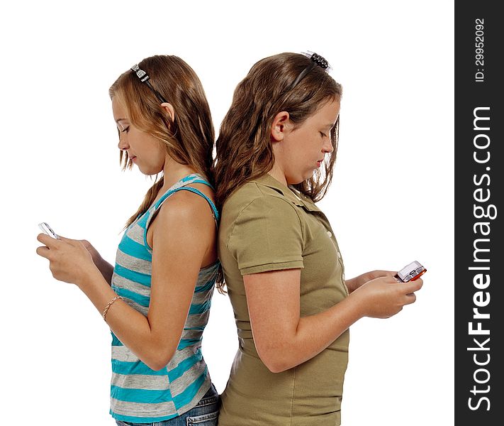 Two teenage girls communicating through text messaging instead of just talking. Sad, but true. Vertical shot, isolated on a white background, shot in studio. Two teenage girls communicating through text messaging instead of just talking. Sad, but true. Vertical shot, isolated on a white background, shot in studio.