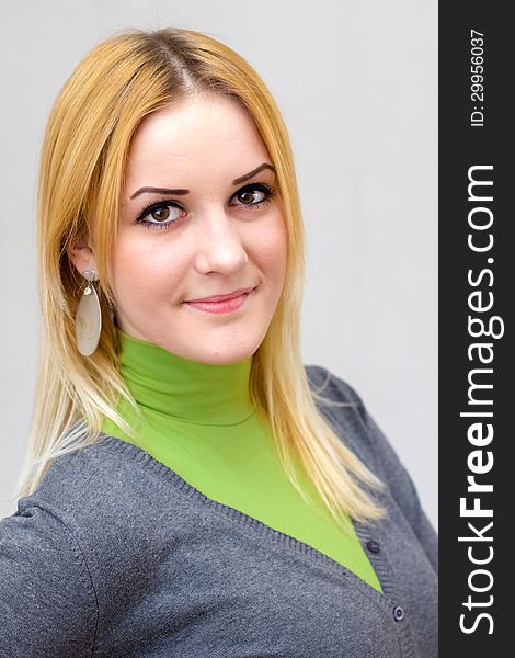 Close-up portrait of a lovely blonde smiling girl with long hair in green turtleneck and gray cardigan