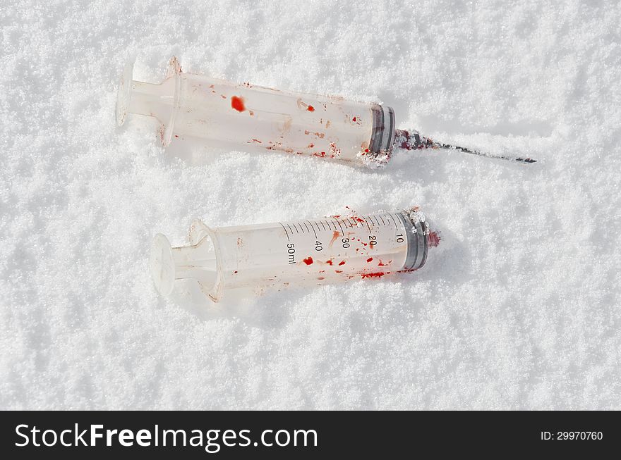 Bloody used syringes on a snowy background