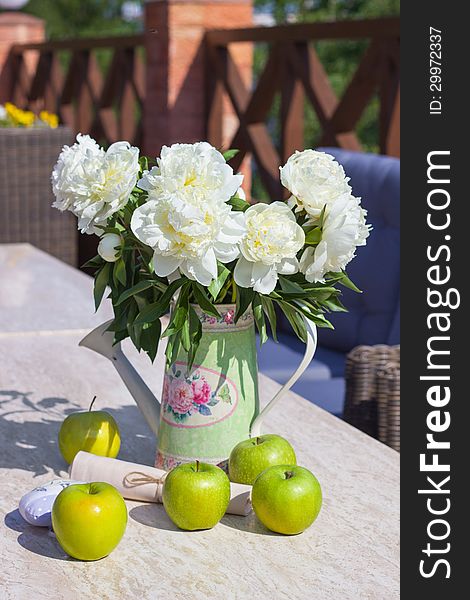 Ripe green apples and a vase of peonies on a table