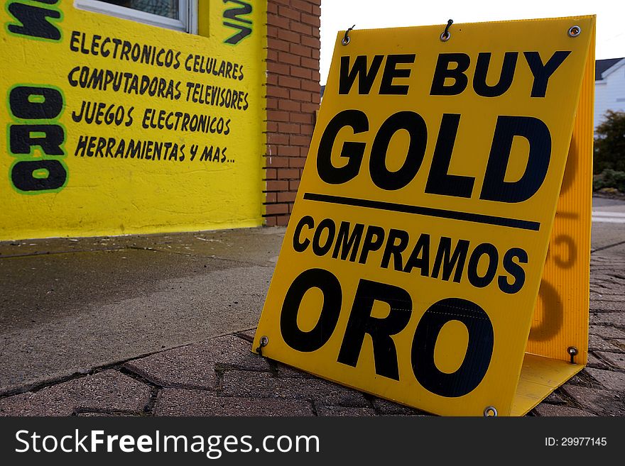 English and Spanish We Buy Gold sign on street with bright yellow wall in background. English and Spanish We Buy Gold sign on street with bright yellow wall in background.