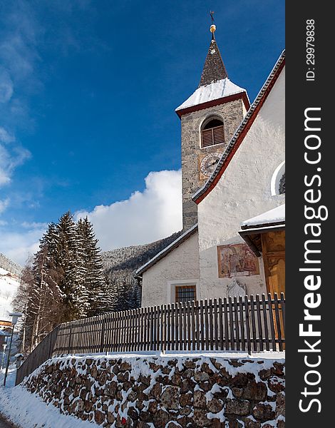 A wintertime view of a small church with a tall steeple in Montassilone, Sud Tyrol