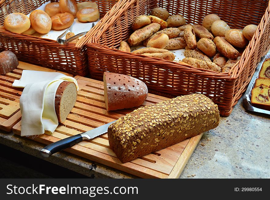 Assortment of baked bread and buns in a basket on wood table