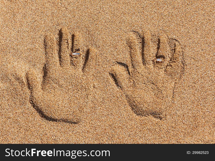 Hand prints on the sand. Hand prints and wedding rings.