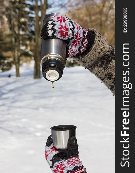 Thermos with the last tea drop and a cup in hands in mittens in winter. Thermos with the last tea drop and a cup in hands in mittens in winter