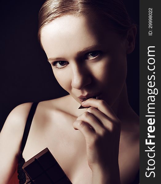 beautiful young woman eating chocolate on a dark background. beautiful young woman eating chocolate on a dark background