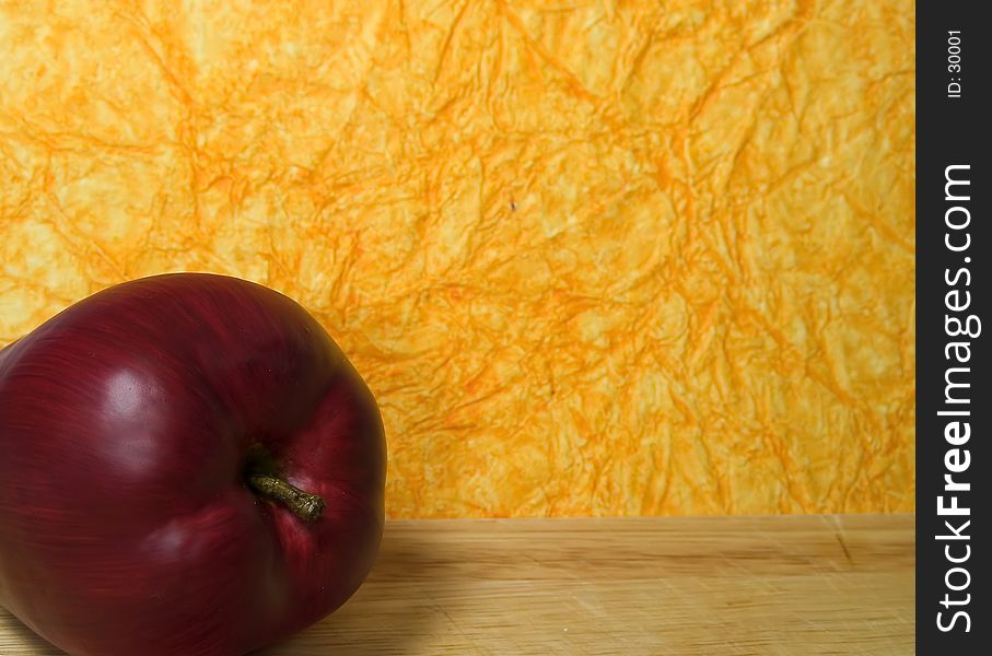 Photo of a Red Apple on a Cutting Board With a Orange Textured Background.