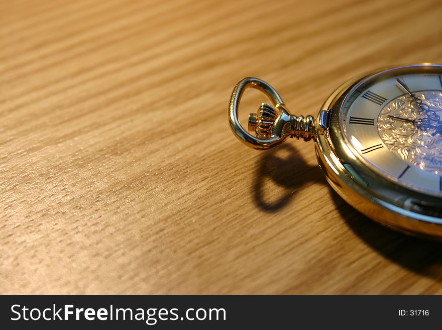 Golden pocket watch against wooden plate. Golden pocket watch against wooden plate.