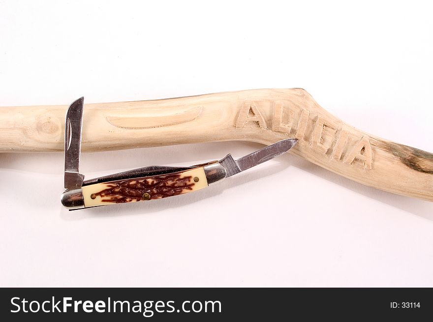 A stick with carvings on it and the knife used to carve the branch lay together on a white background. A stick with carvings on it and the knife used to carve the branch lay together on a white background.