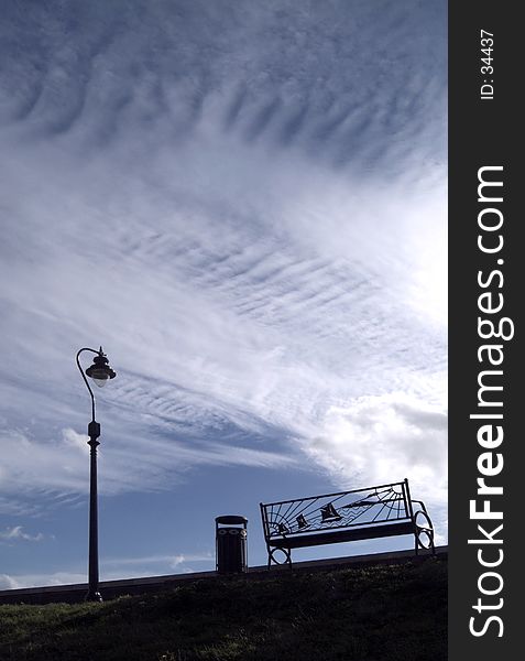 Unusual public seat with streetlight and wastebin silhouetted against a dramatic sky. Location: Tilbury, Essex, UK. Unusual public seat with streetlight and wastebin silhouetted against a dramatic sky. Location: Tilbury, Essex, UK