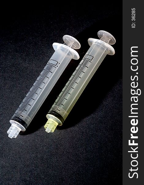 A pair of syringes photographed on a black background. A pair of syringes photographed on a black background