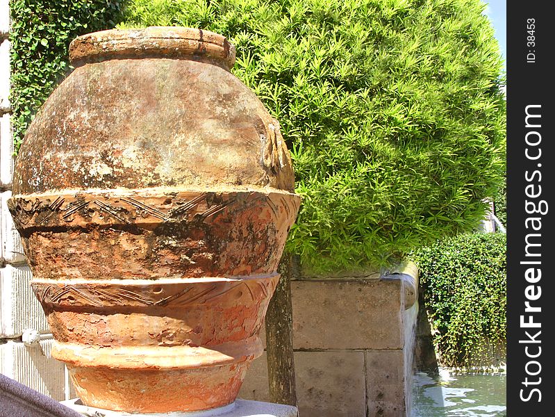 Red clay pot next to globularly-shaped tree, in garden of museum. Red clay pot next to globularly-shaped tree, in garden of museum