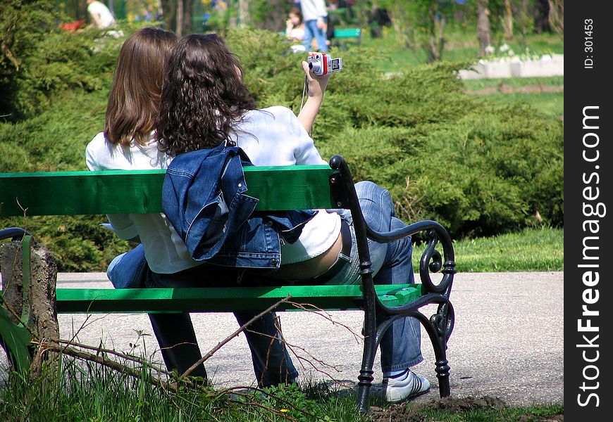 Two girls on a bench in a park taking a photo of themself