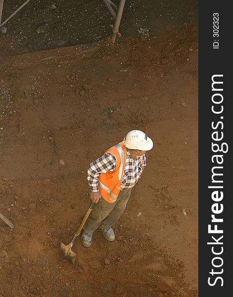 A workman leans on his shovel in a dirt pit. A workman leans on his shovel in a dirt pit