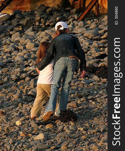 A young girl standing on a pebble beach, with her arm protectively around a younger child,