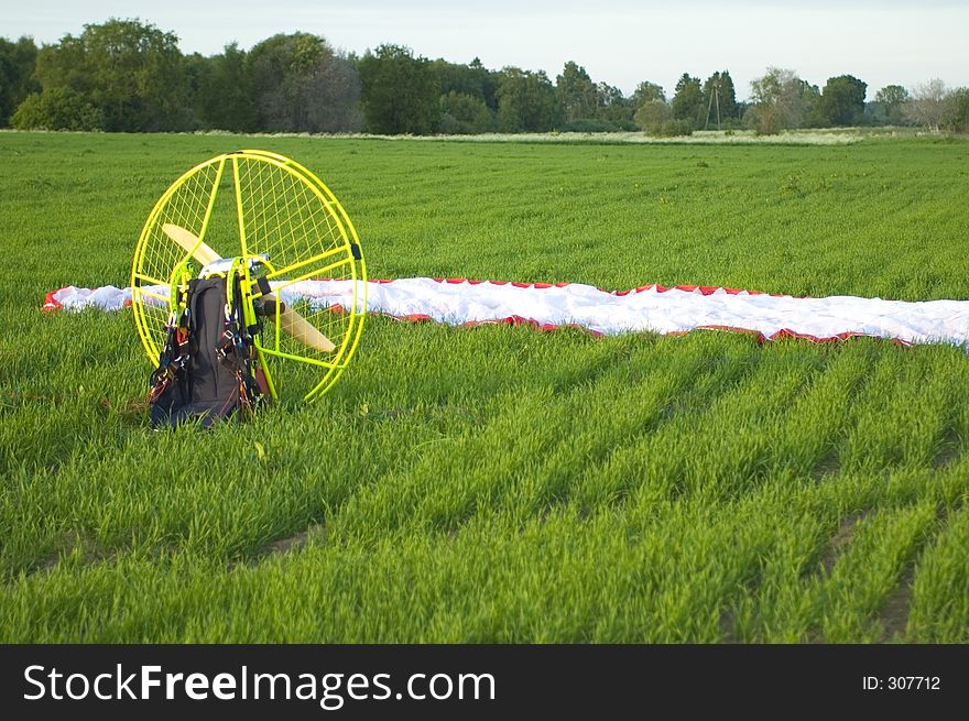 Parachute resting on grass, motorised backpack used for flying the thing is in the foreground.