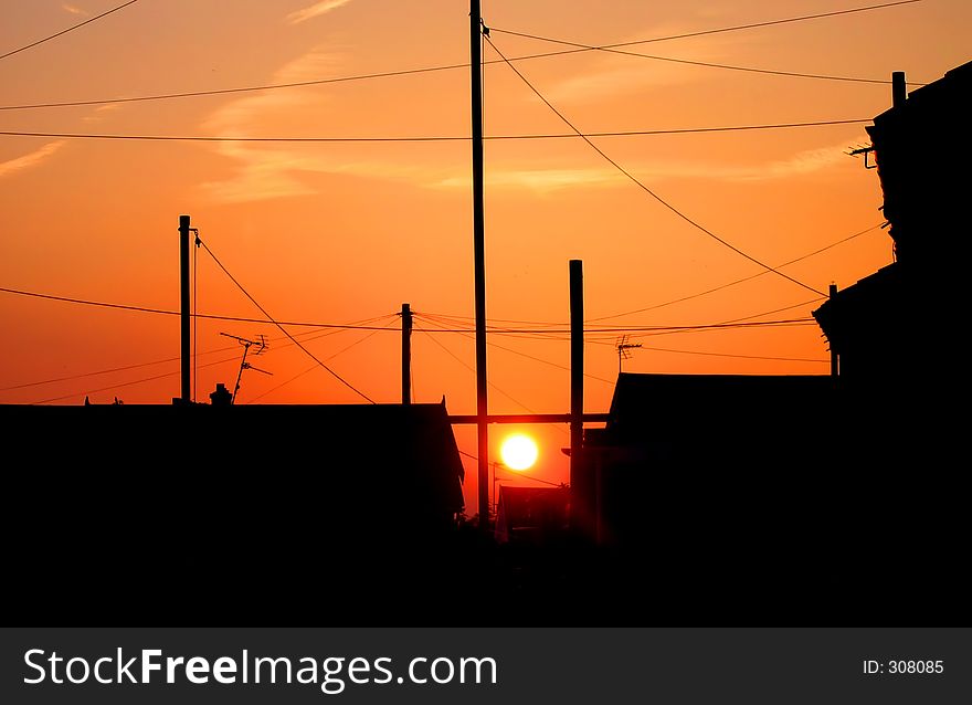 Sunset in residential area with silhouettes of houses and telephone poles and lines. Sunset in residential area with silhouettes of houses and telephone poles and lines