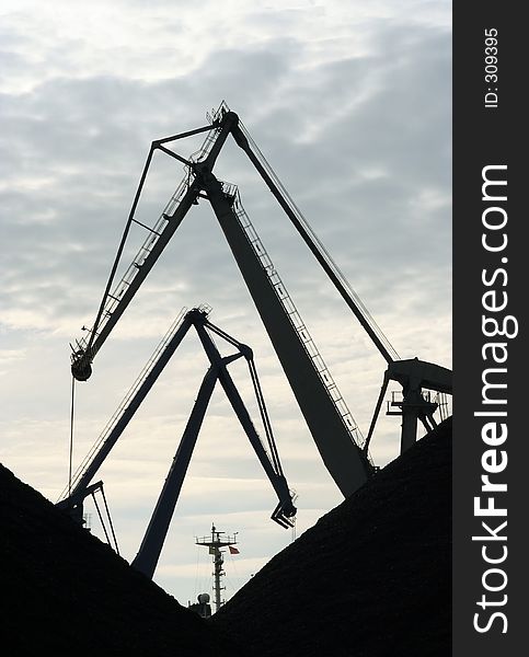 Crane silhouettes in a harbour. Piles of coal in front. Crane silhouettes in a harbour. Piles of coal in front